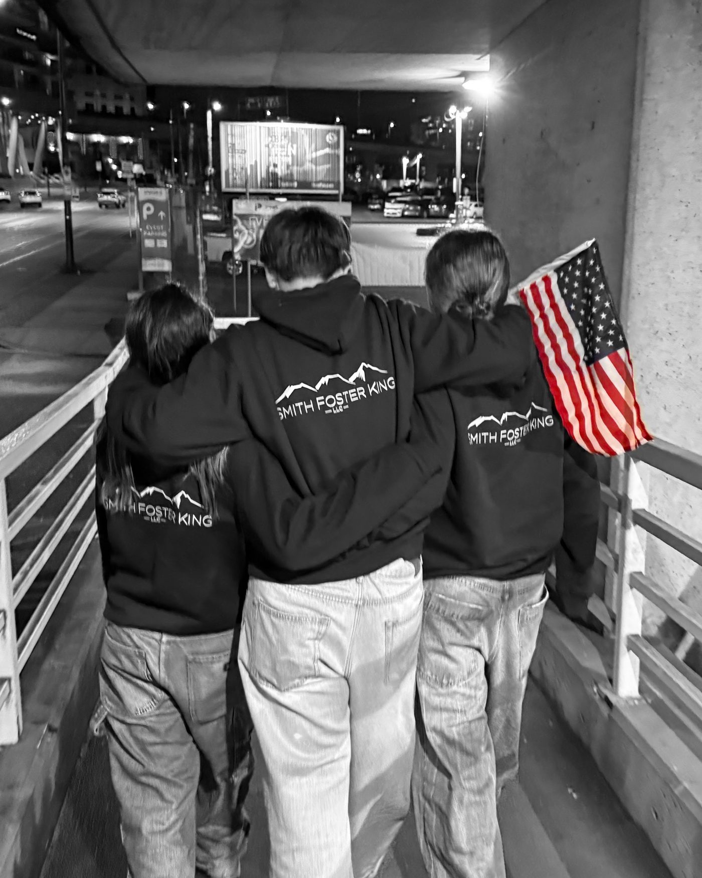 Three young rugby players in Smith Foster King sweatshirts walking arm in arm with an American flag